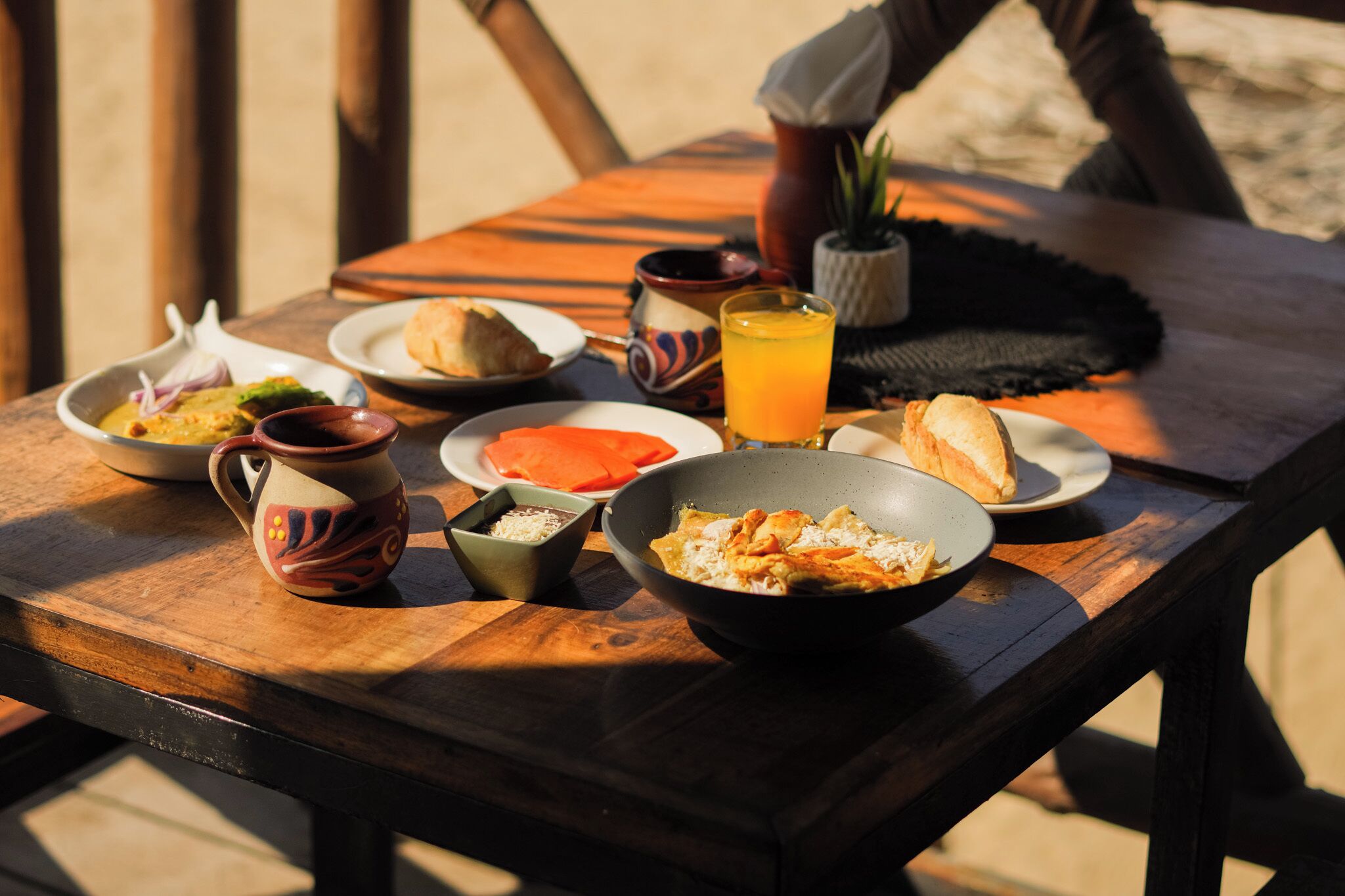 Una mesa de madera con diversos platos, incluyendo un tazón de arroz, una rebanada de pan y un vaso de jugo de naranja.