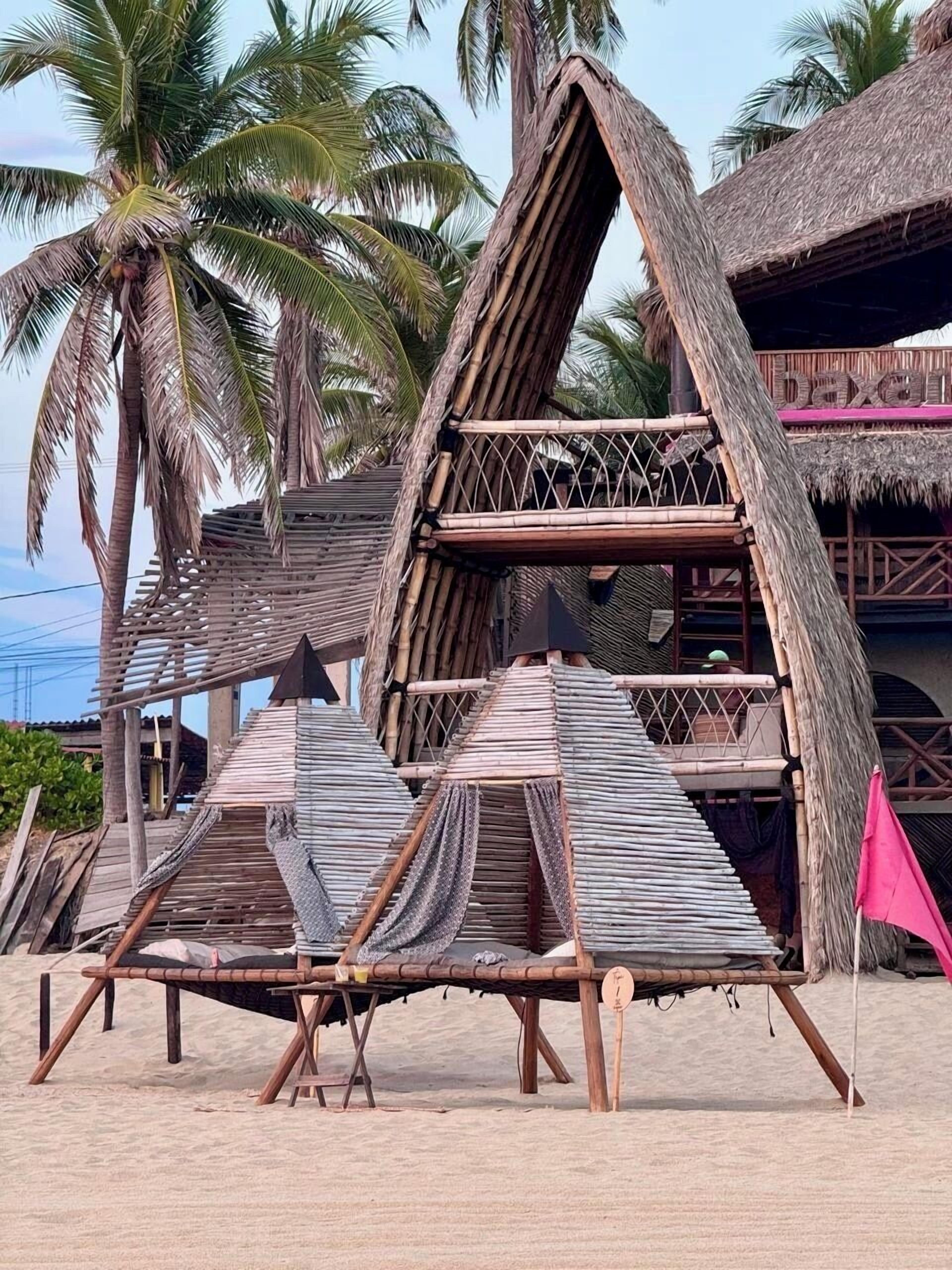 A beach hut with a thatched roof, bamboo walls, and a small balcony.