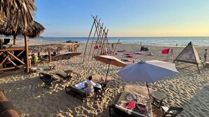 A beach with sun loungers, umbrellas, and a thatched structure. - Hotel BaXar (Acapulco)