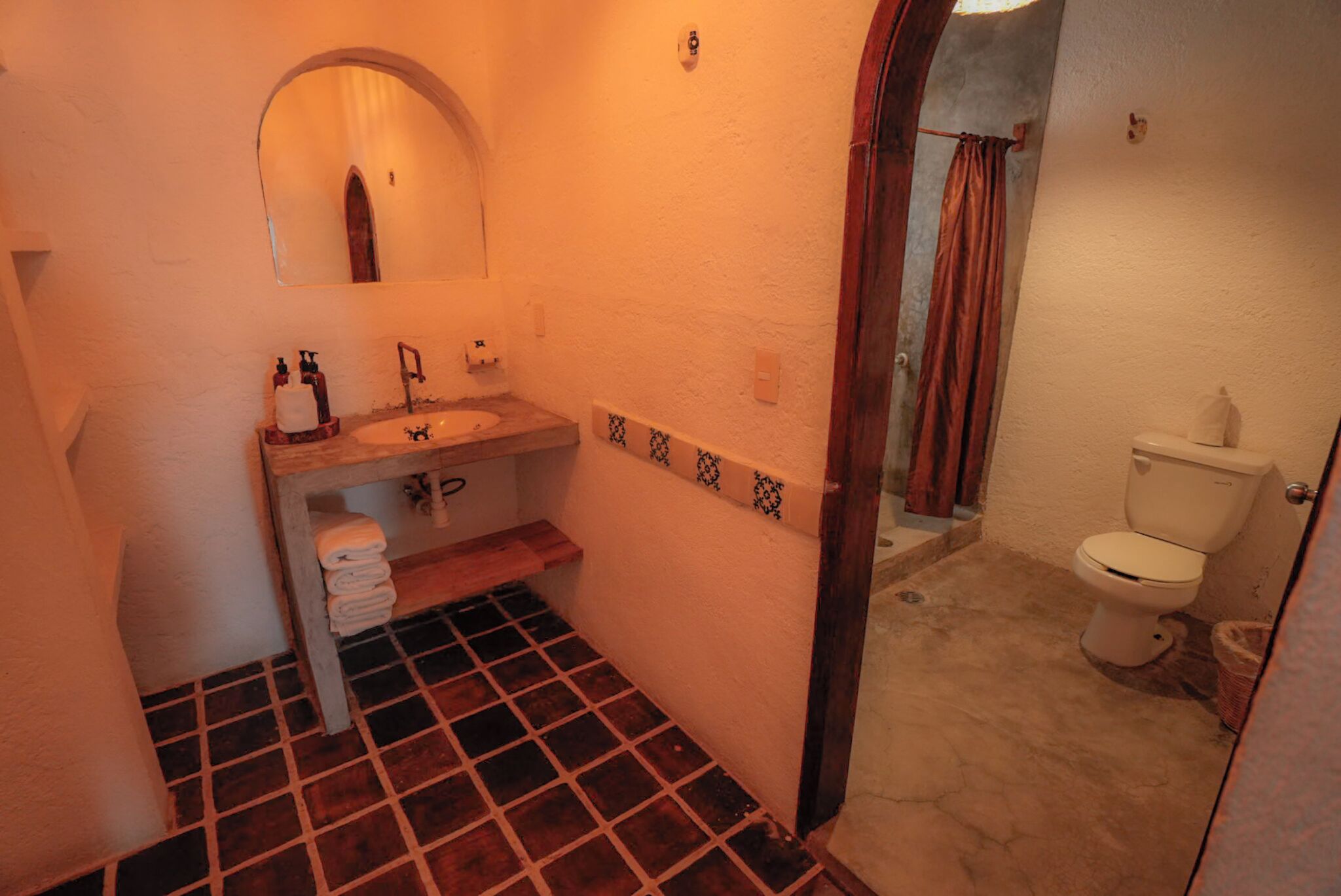 A bathroom with a tiled floor, a sink with a mirror above it, a toilet, and a shower area with a curtain.