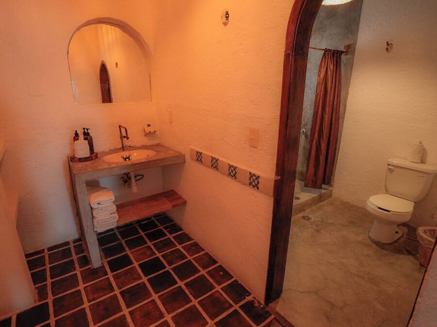 A bathroom with a tiled floor, a sink with a mirror above it, a toilet, and a shower area with a curtain.