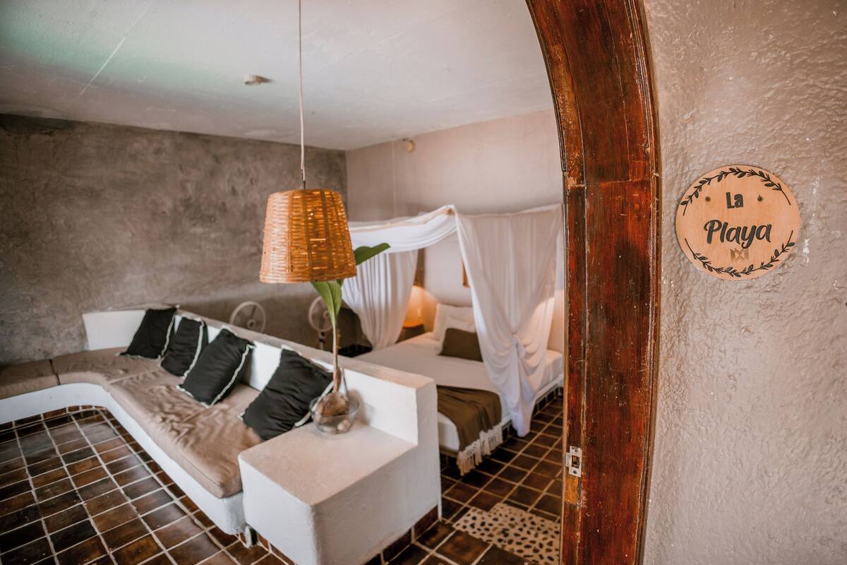 A bedroom with a bed, a sofa, a hanging light fixture, and a wall-mounted sign.