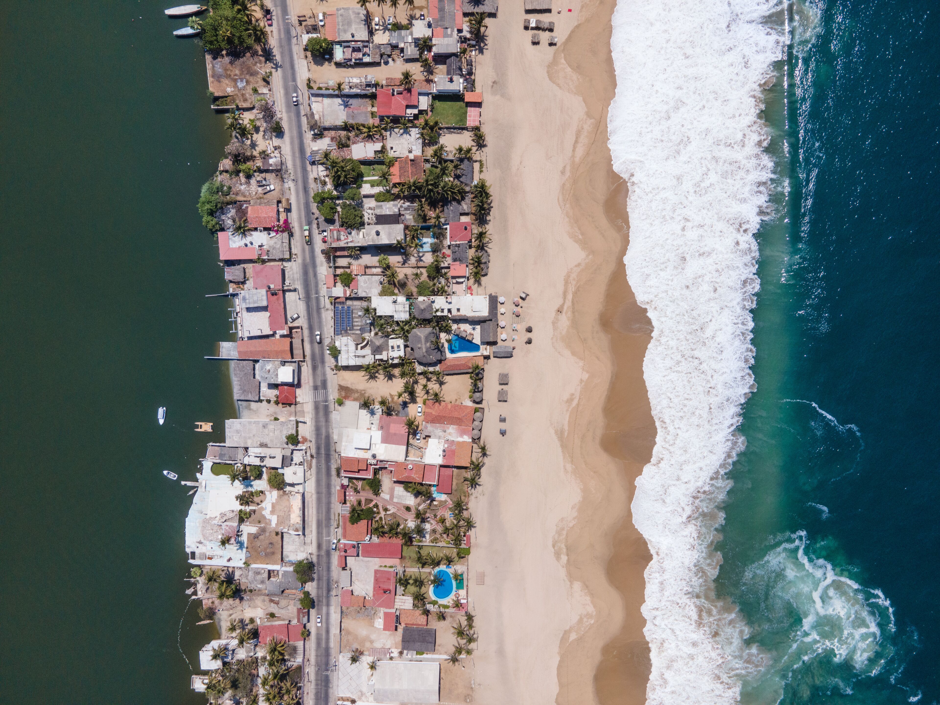 An aerial view of a coastal area with buildings, a beach, and a swimming pool.