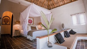 A room with a bed, a sofa, a fan, a plant, and a thatched roof. - Hotel BaXar (Acapulco)