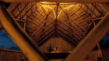 Una estructura de techo de paja con una zona de estar central y vistas al exterior.