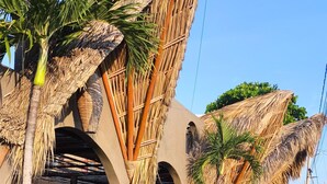 A row of buildings with thatched roofs and palm trees lining a paved walkway. - Hotel BaXar (Acapulco)