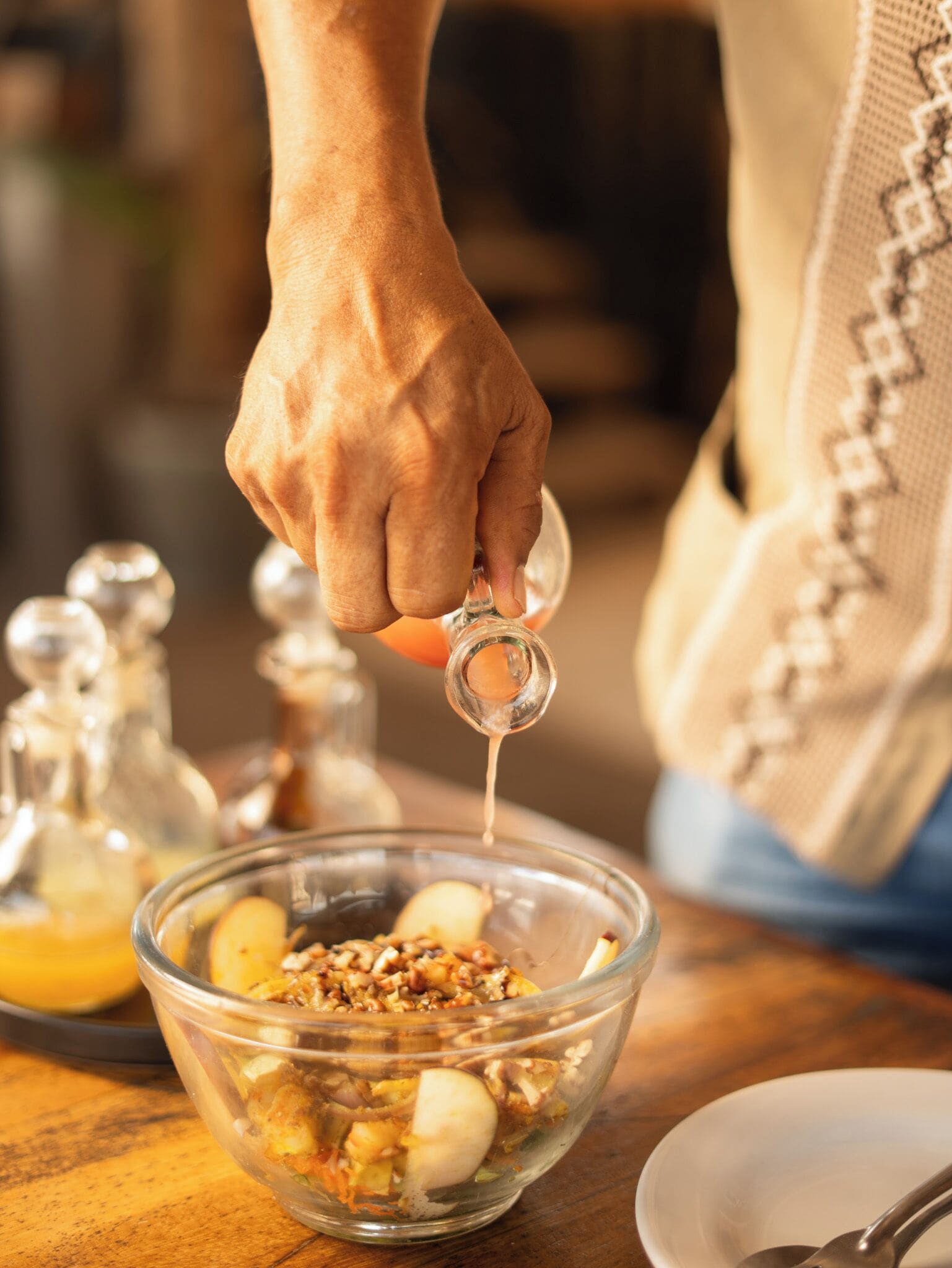 A person pouring a clear liquid into a glass bowl containing food ingredients.