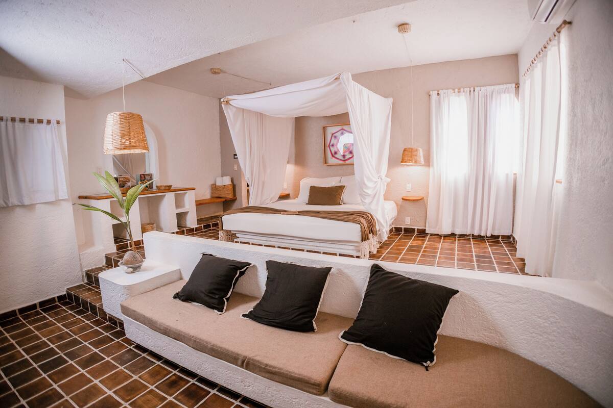 A bedroom with a canopy bed, a sofa with cushions, a bedside table, and a lamp.