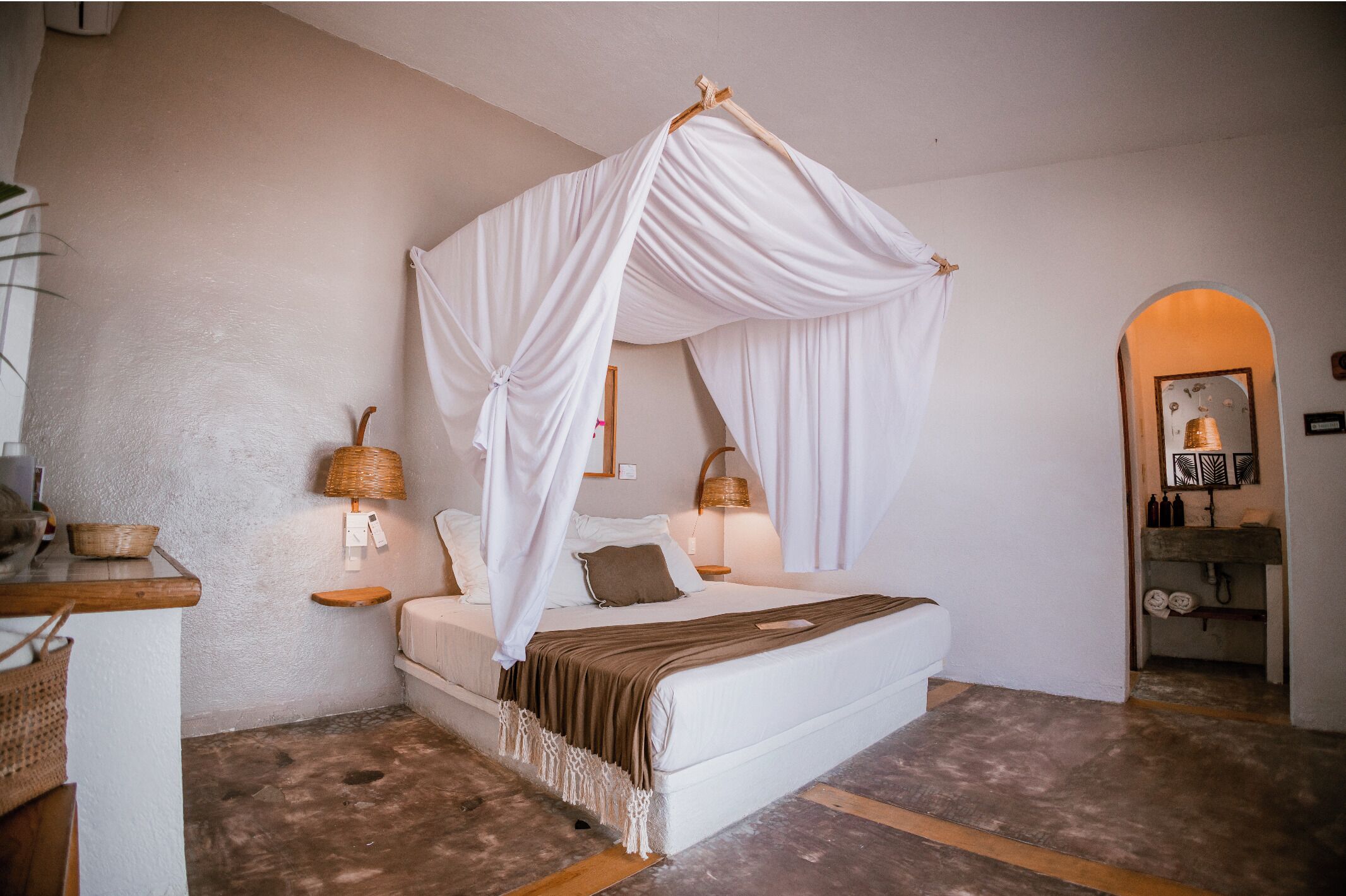 A bedroom with a four-poster canopy bed, bedside tables with lamps, a small shelf, and a wooden floor.
