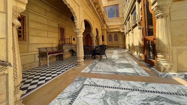 Un patio ornamentado con piso a cuadros, columnas labradas y muebles de madera tradicionales.