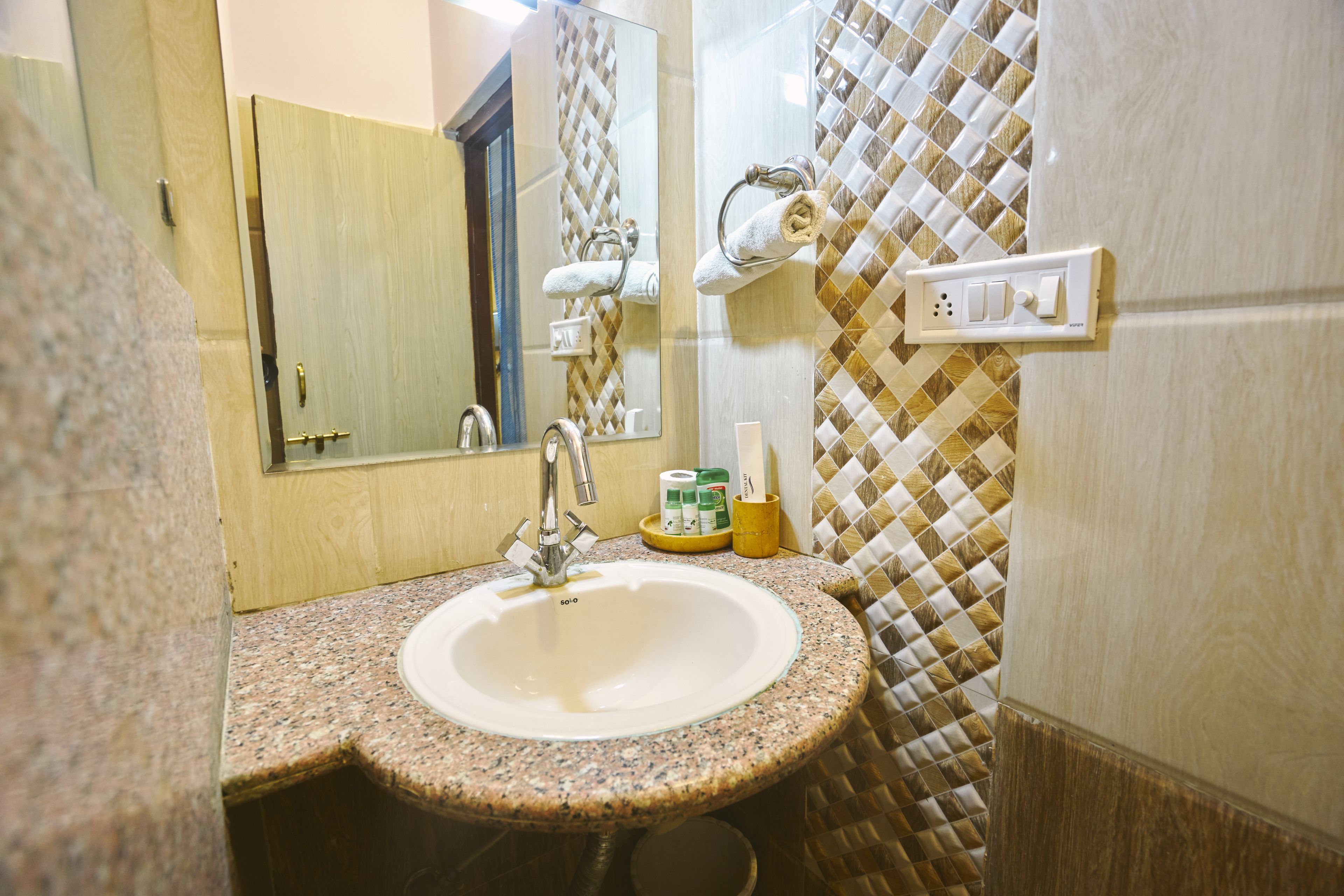 Une salle de bain avec un lavabo doté d’un plan de travail en granit, un miroir, un porte-serviettes et un interrupteur fixé au mur.