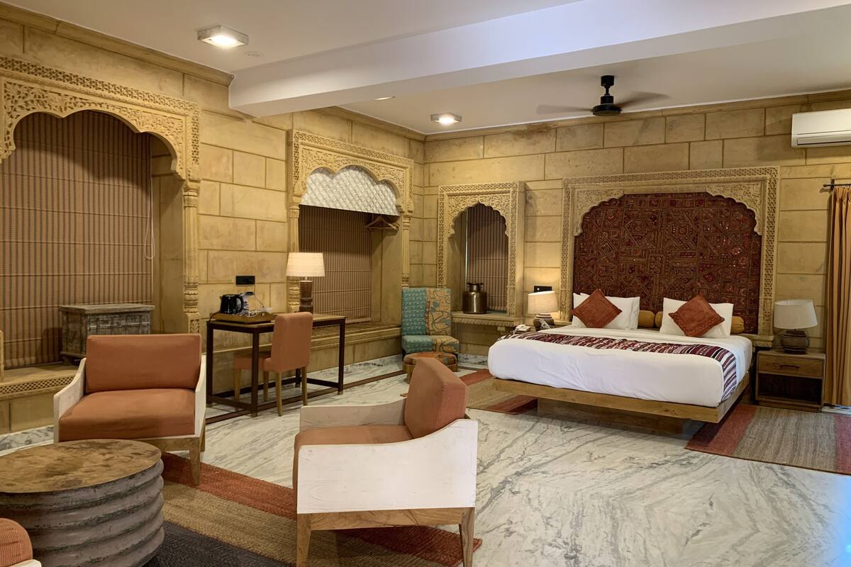 Een hotelkamer met een groot bed, twee fauteuils, een klein tafeltje en een decoratief hoofdeinde.