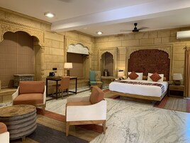 A hotel room with a large bed, two armchairs, a small table, and a decorative headboard.