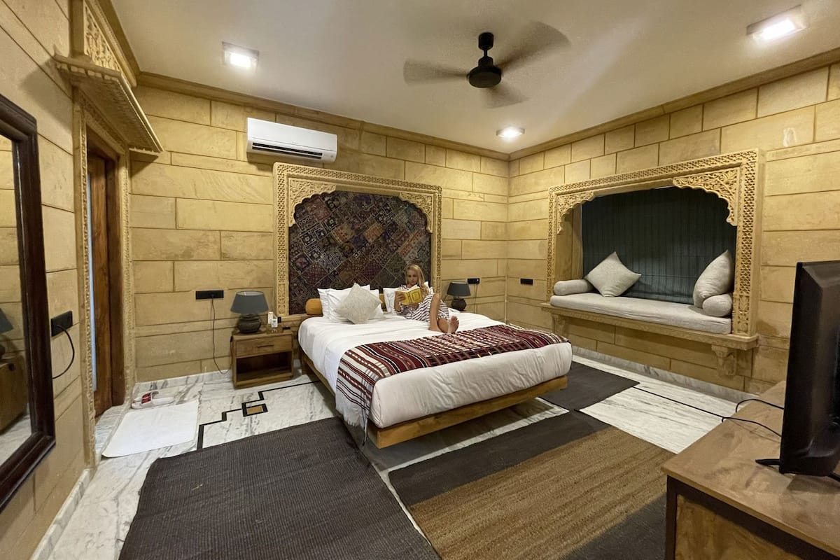 Een hotelkamer met een bed, een leestoel, een televisie en een airconditioning.