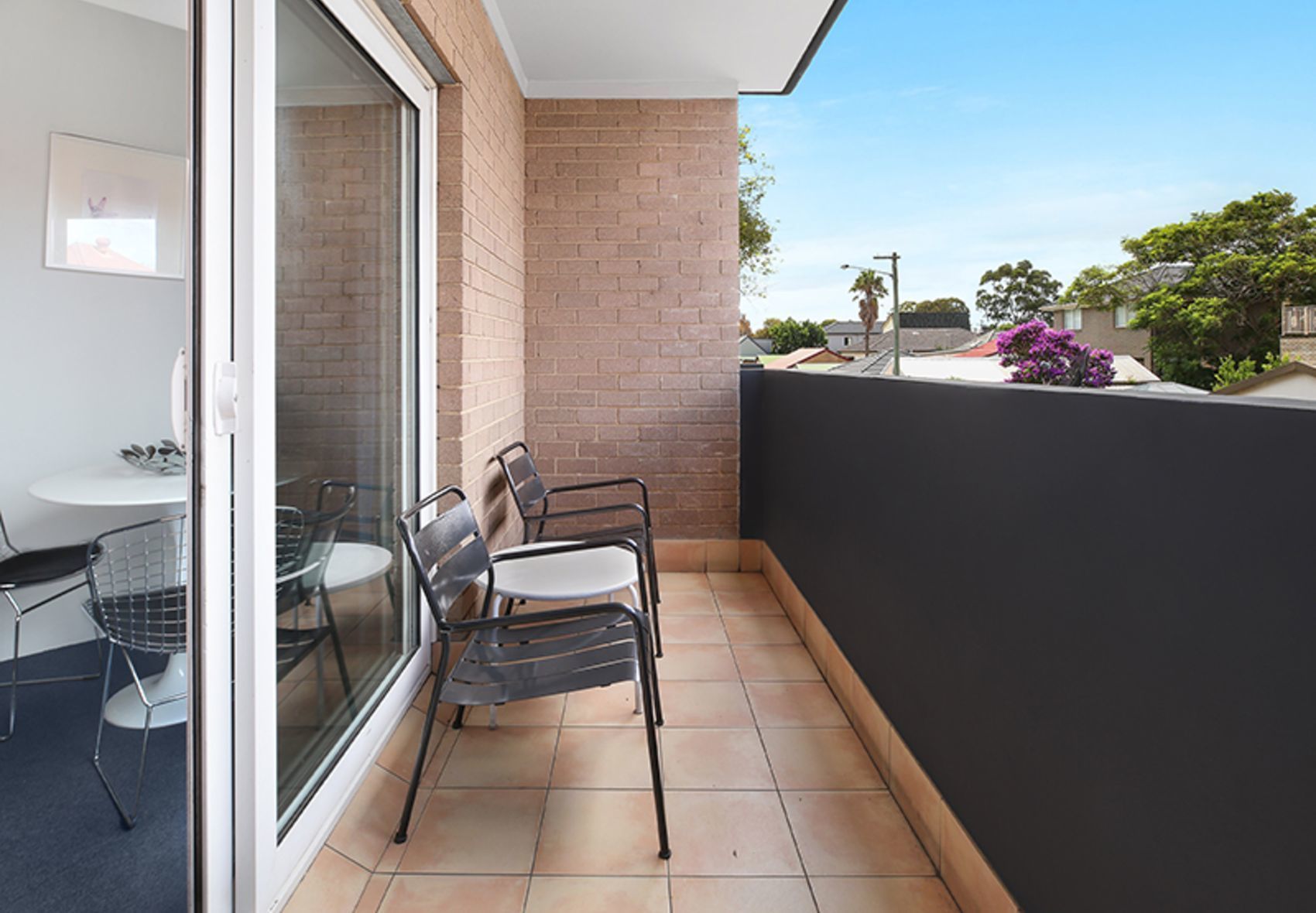 A balcony with a table and chairs, a glass door, and a view of the neighborhood.