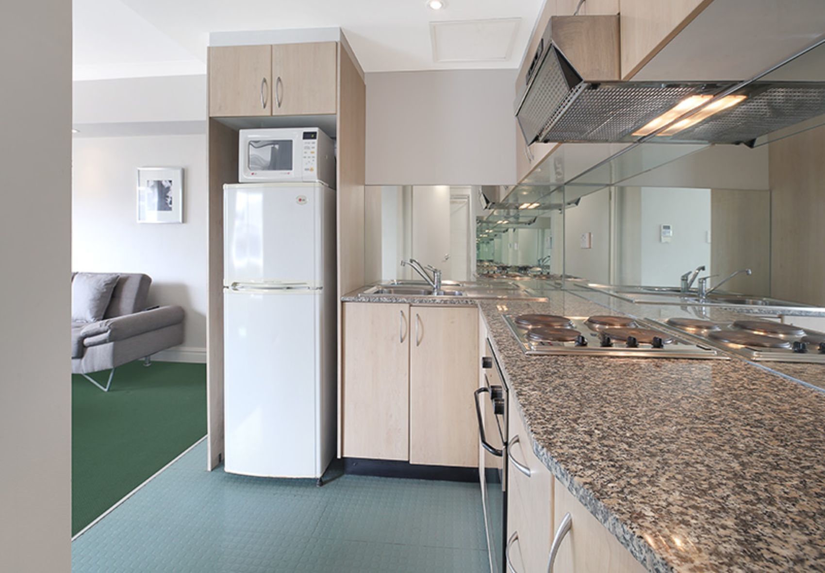 A compact kitchen with a built-in microwave, a refrigerator, a sink, and a granite countertop.