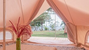 A tented accommodation with a bed, a green vase with red plants, and a view of a grassy area and trees. - Soka Indah Restaurant & Bungalows (Selemadeg)