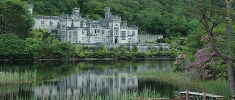 A historic castle with a moat and boats, surrounded by lush greenery.