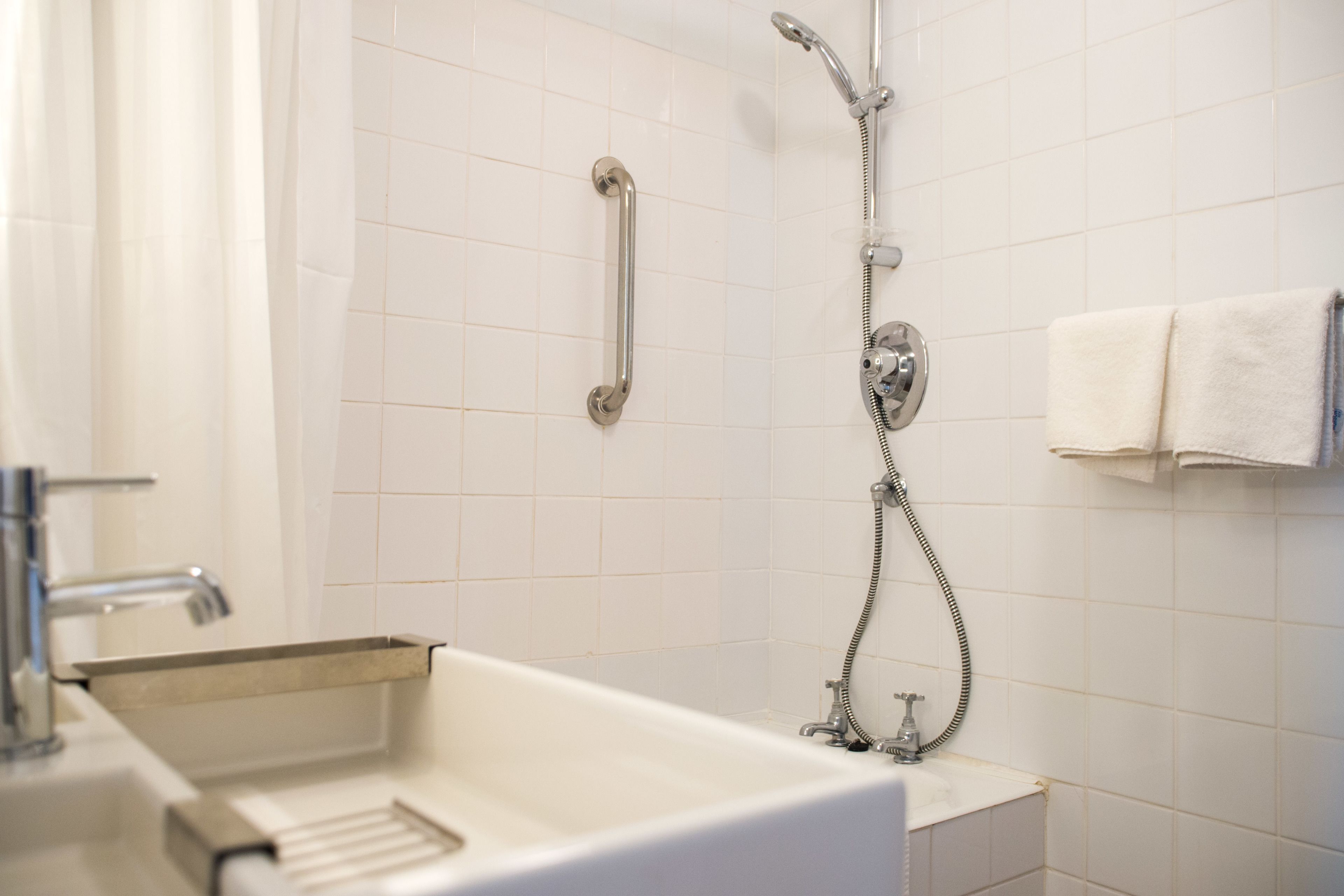 Un baño con un lavamanos blanco, un cabezal de ducha de mano y un perchero para toallas.