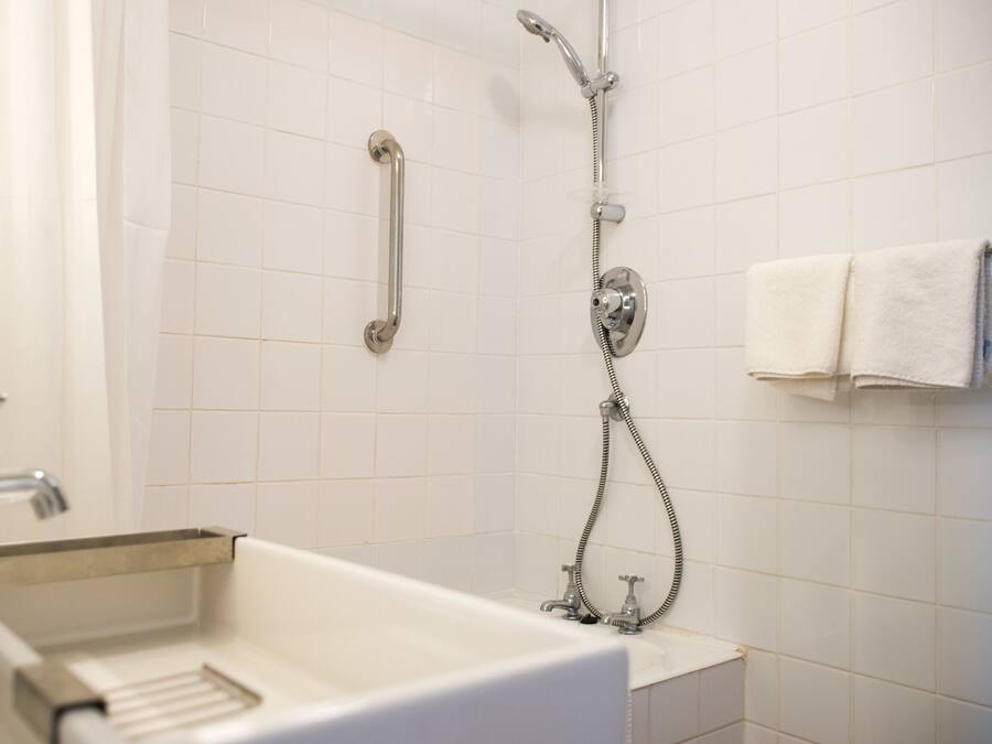 Un baño con un lavamanos blanco, un cabezal de ducha de mano y un perchero para toallas.