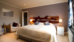 A bedroom with a large bed, two bedside tables with lamps, a chair, a wooden headboard, and a mirror on the wall. - Sharamore House (Clifden)