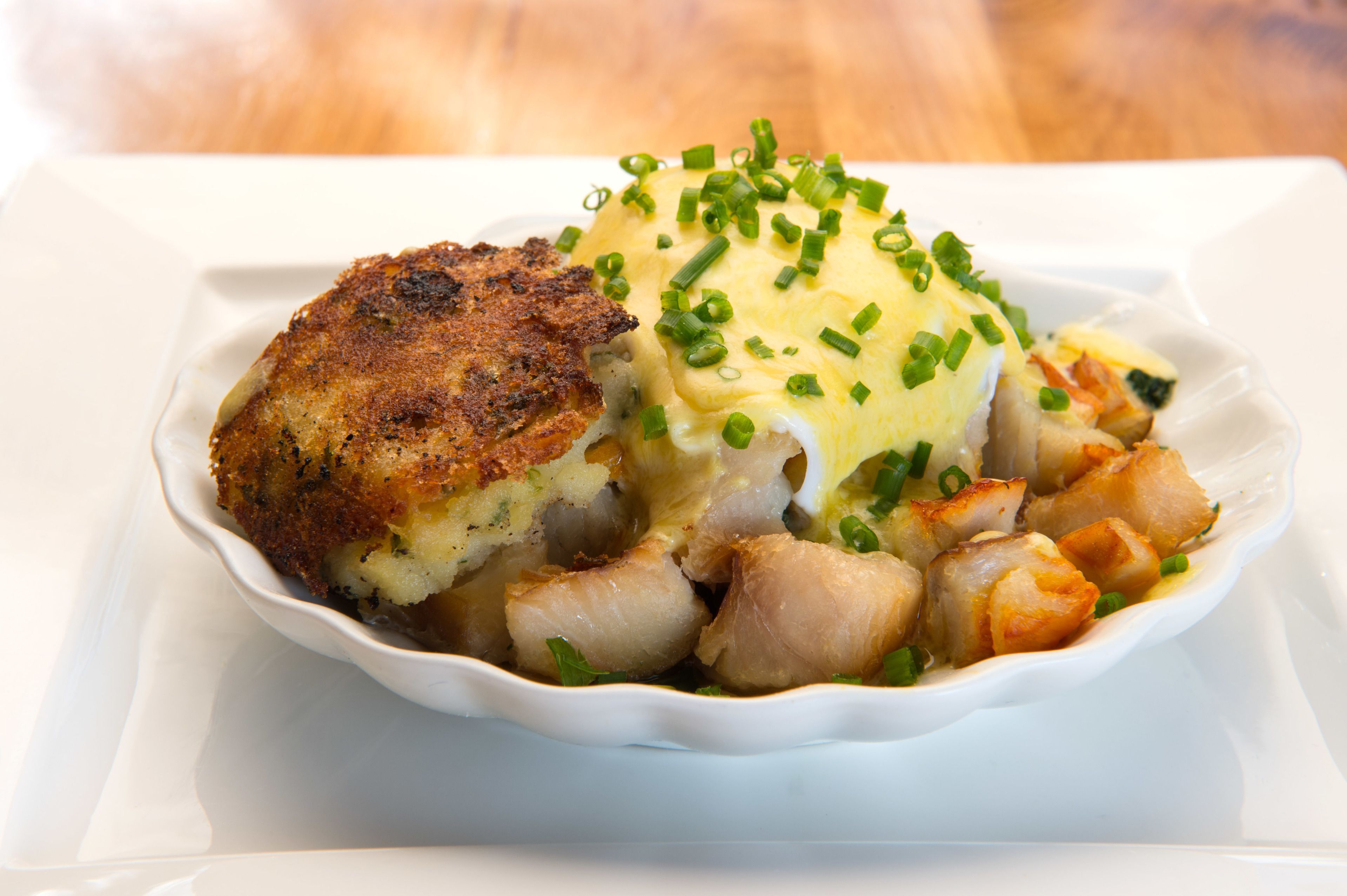 A white ceramic dish containing a breaded item, possibly a fish fillet, and a creamy sauce garnished with green onions.