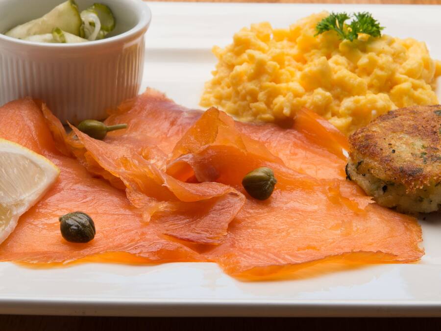 A plate with smoked salmon, capers, lemon, scrambled eggs, and a small salad.
