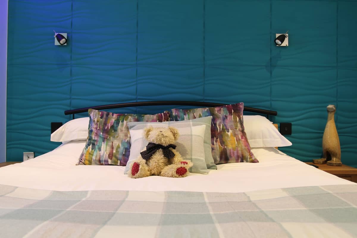 Cama com um urso de pelúcia, almofadas estampadas e cabeceira azul.