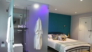 Un dormitorio moderno con cama, mesita de noche, espejo y baño con inodoro y ducha.