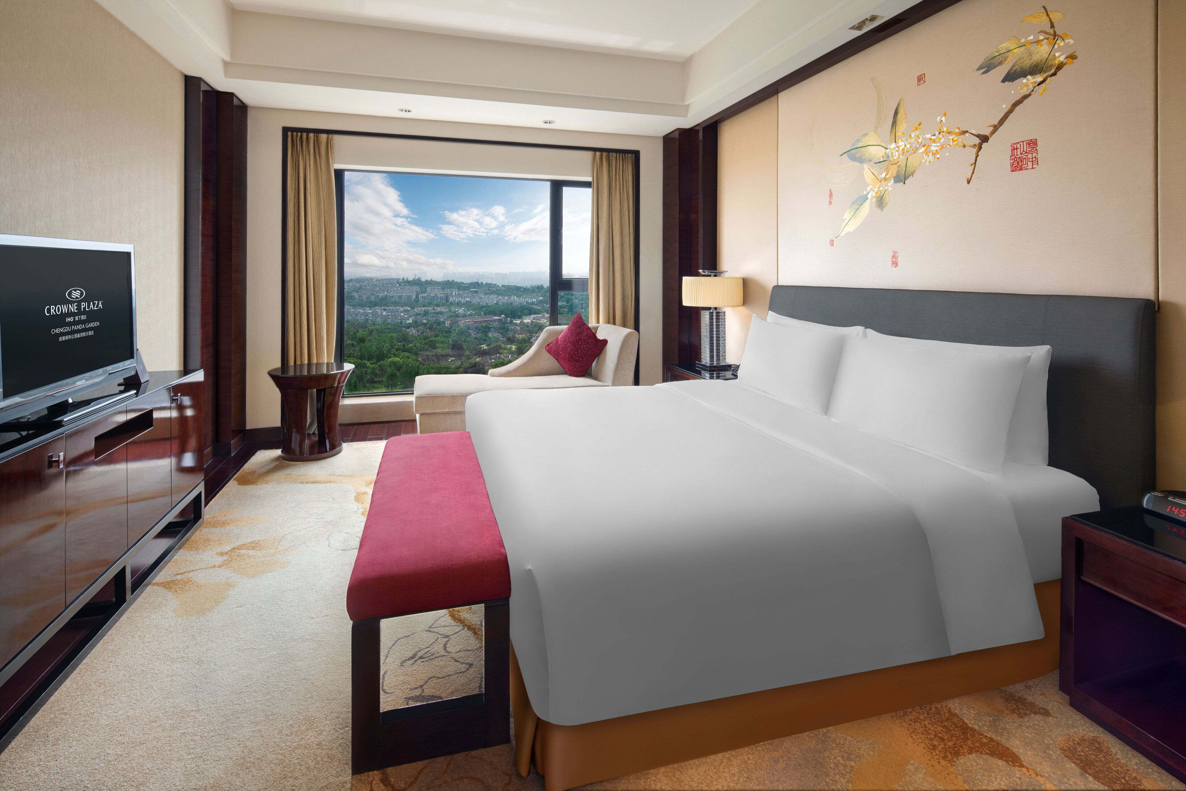 A hotel room with a large bed, a television, a desk, and a view of the city.
