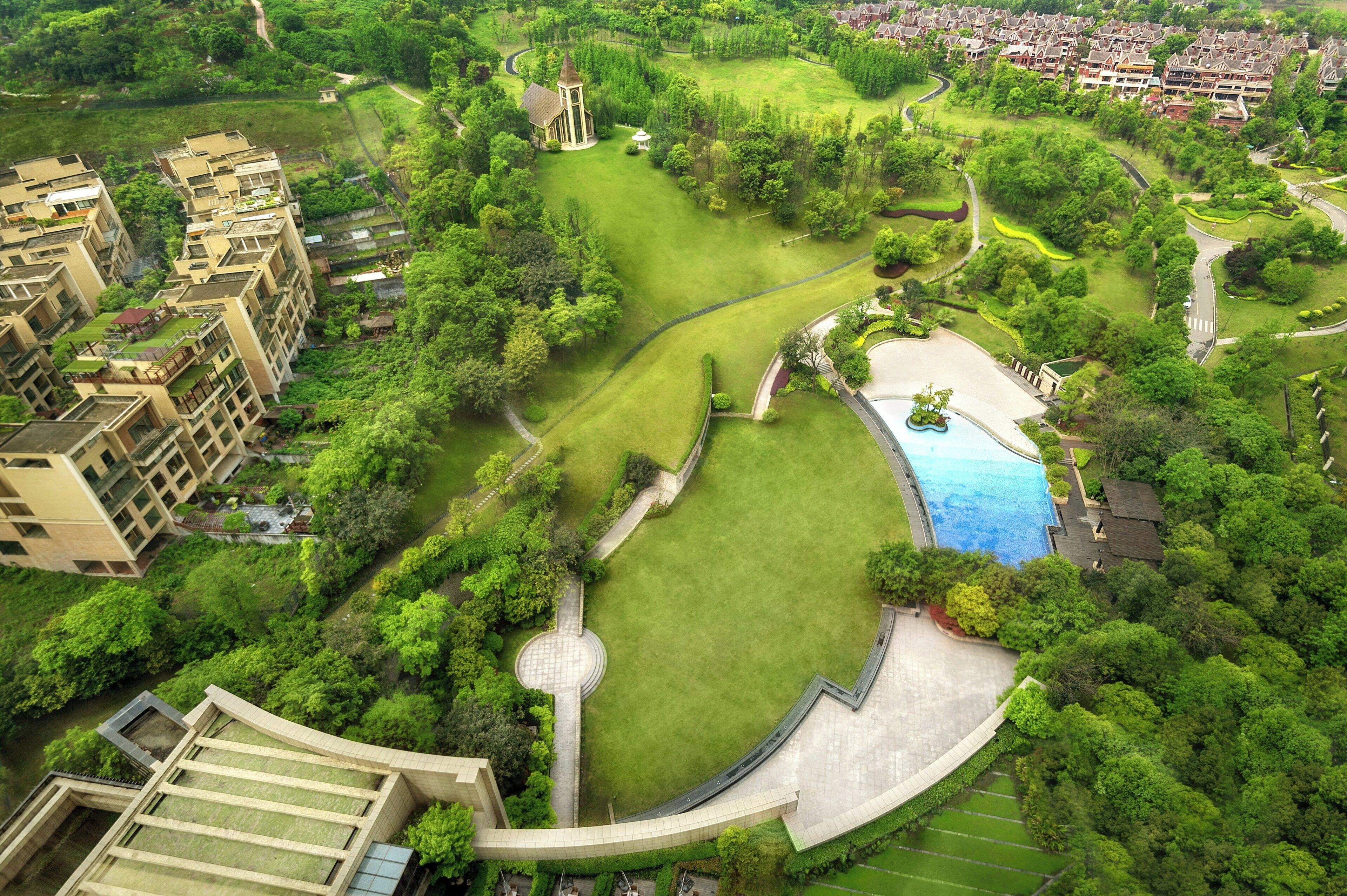 An aerial view of a residential area with a swimming pool, green lawns, and a church.