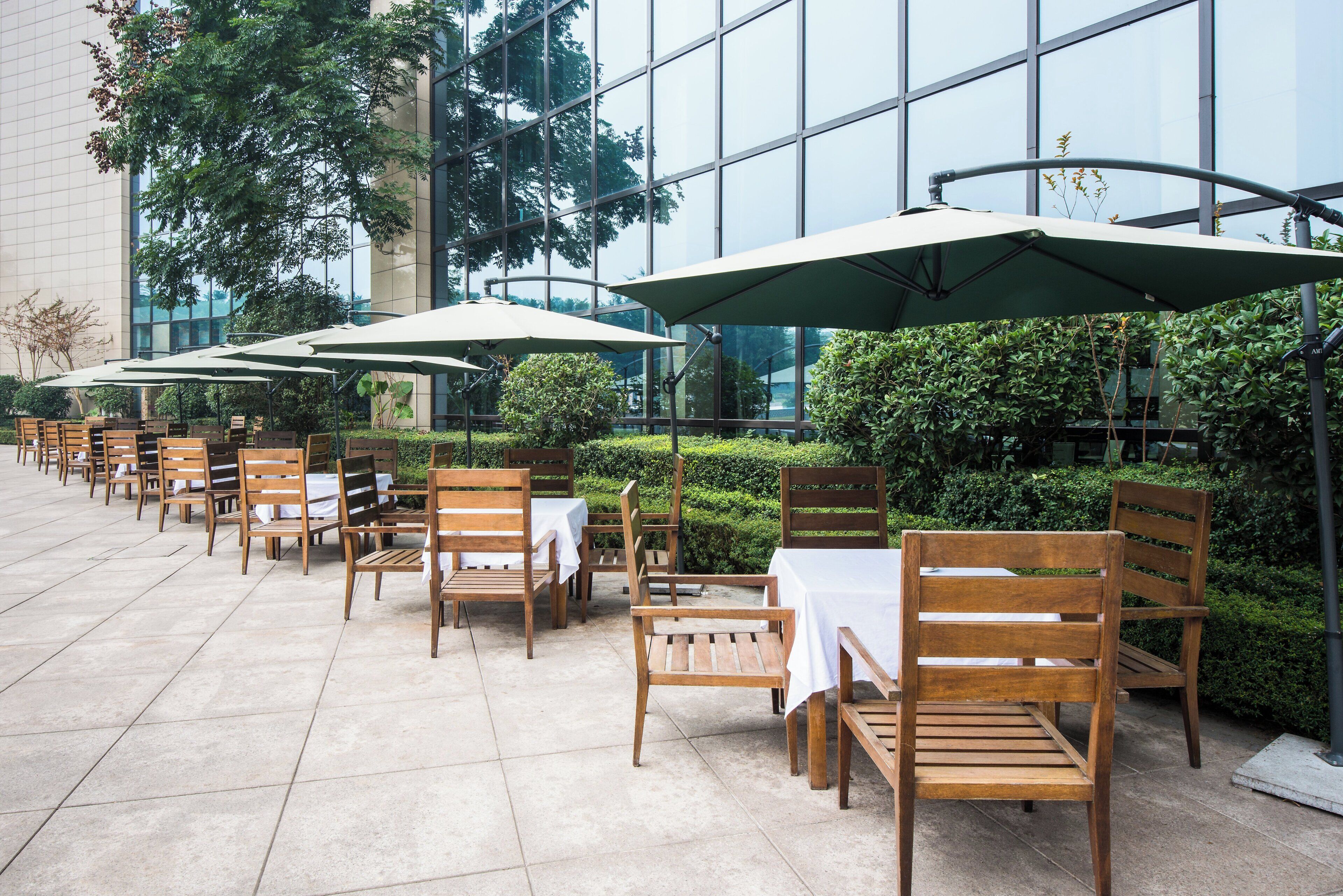 Buiten zitplaatsen met tafels en stoelen, parasols, en een gebouw met grote ramen op de achtergrond.