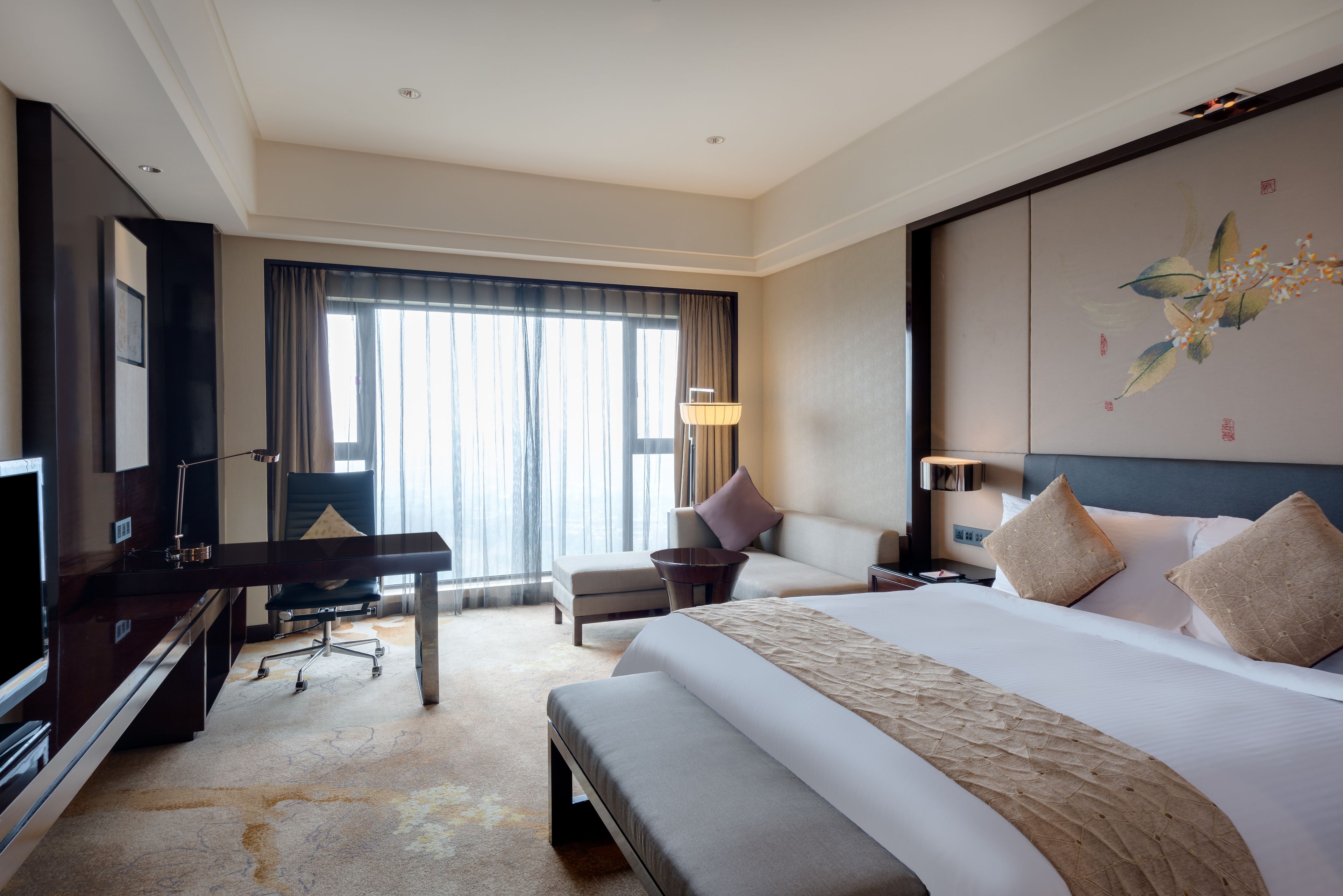 A hotel room with a large bed, a desk with a chair, a TV, and a large window with curtains.