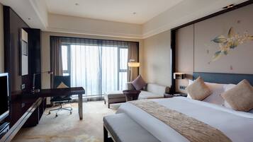A hotel room with a large bed, a desk with a chair, a TV, and a large window with curtains.