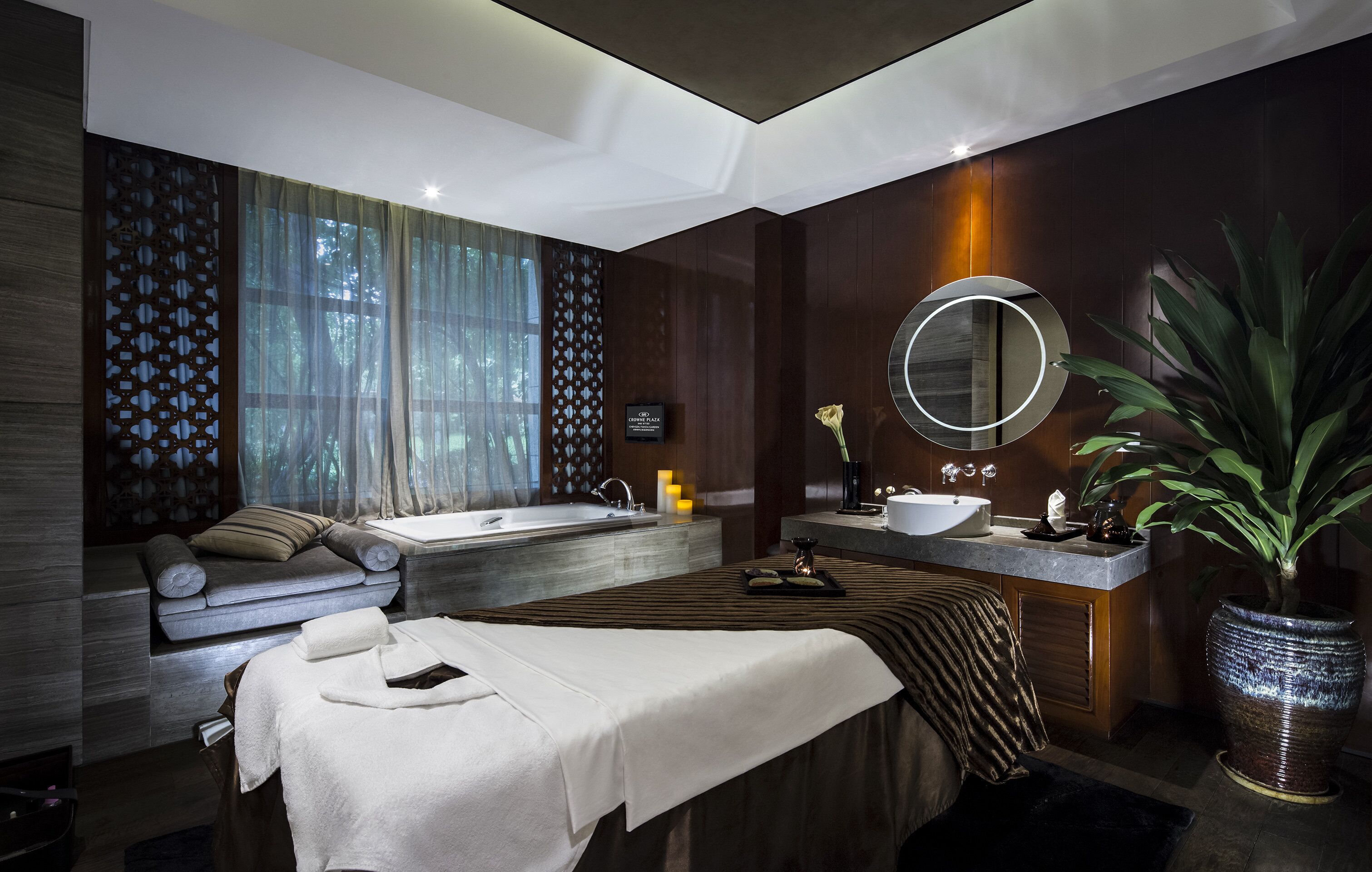 A modern spa room with a large bathtub, a massage table, and a sink.