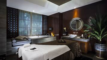 A modern spa room with a large bathtub, a massage table, and a sink.