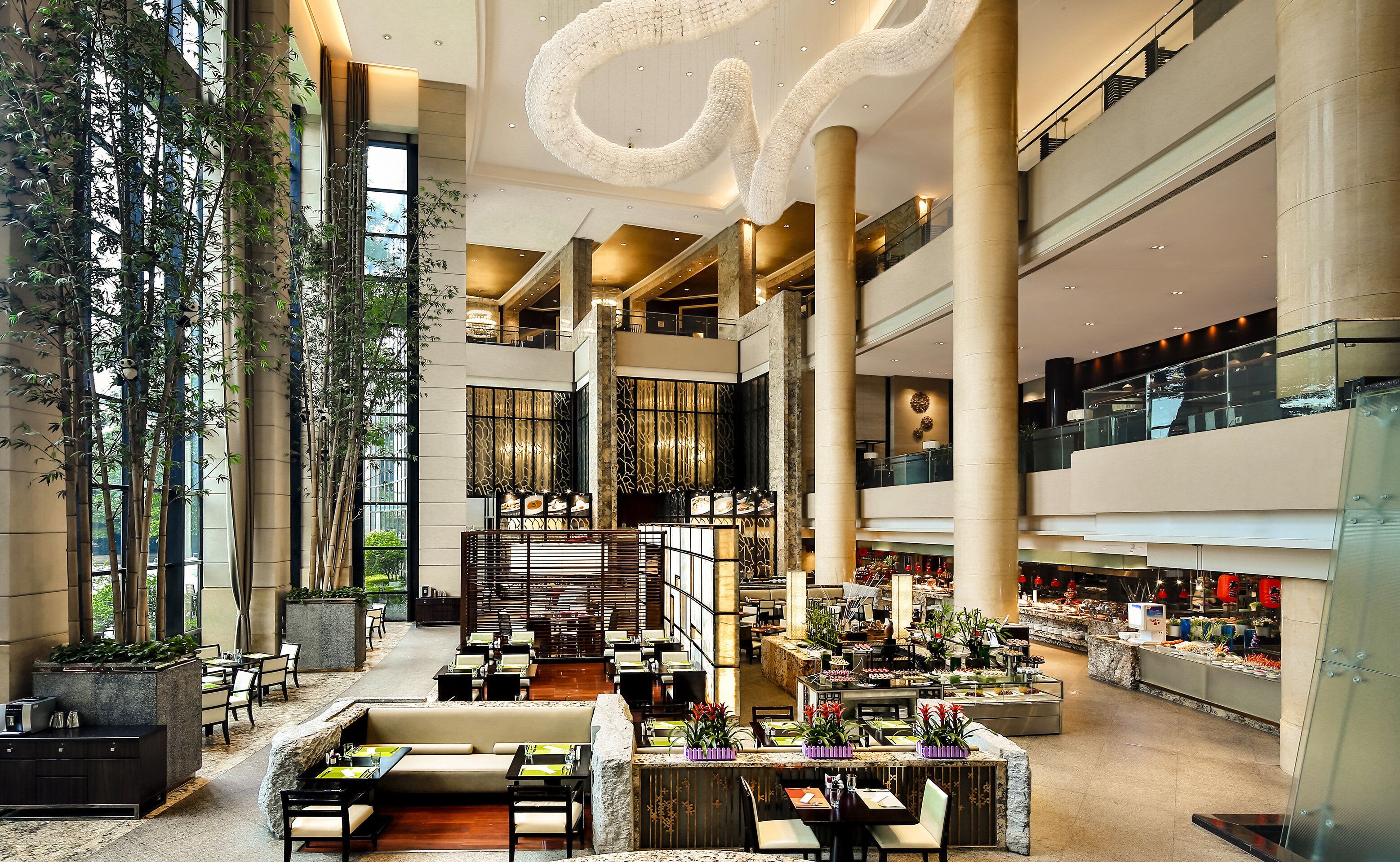 A spacious hotel lobby with multiple dining areas, high ceilings, and large windows.