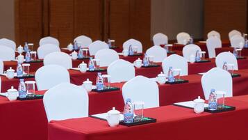 A conference room with rows of white chairs, red tablecloths, and water bottles on each table.