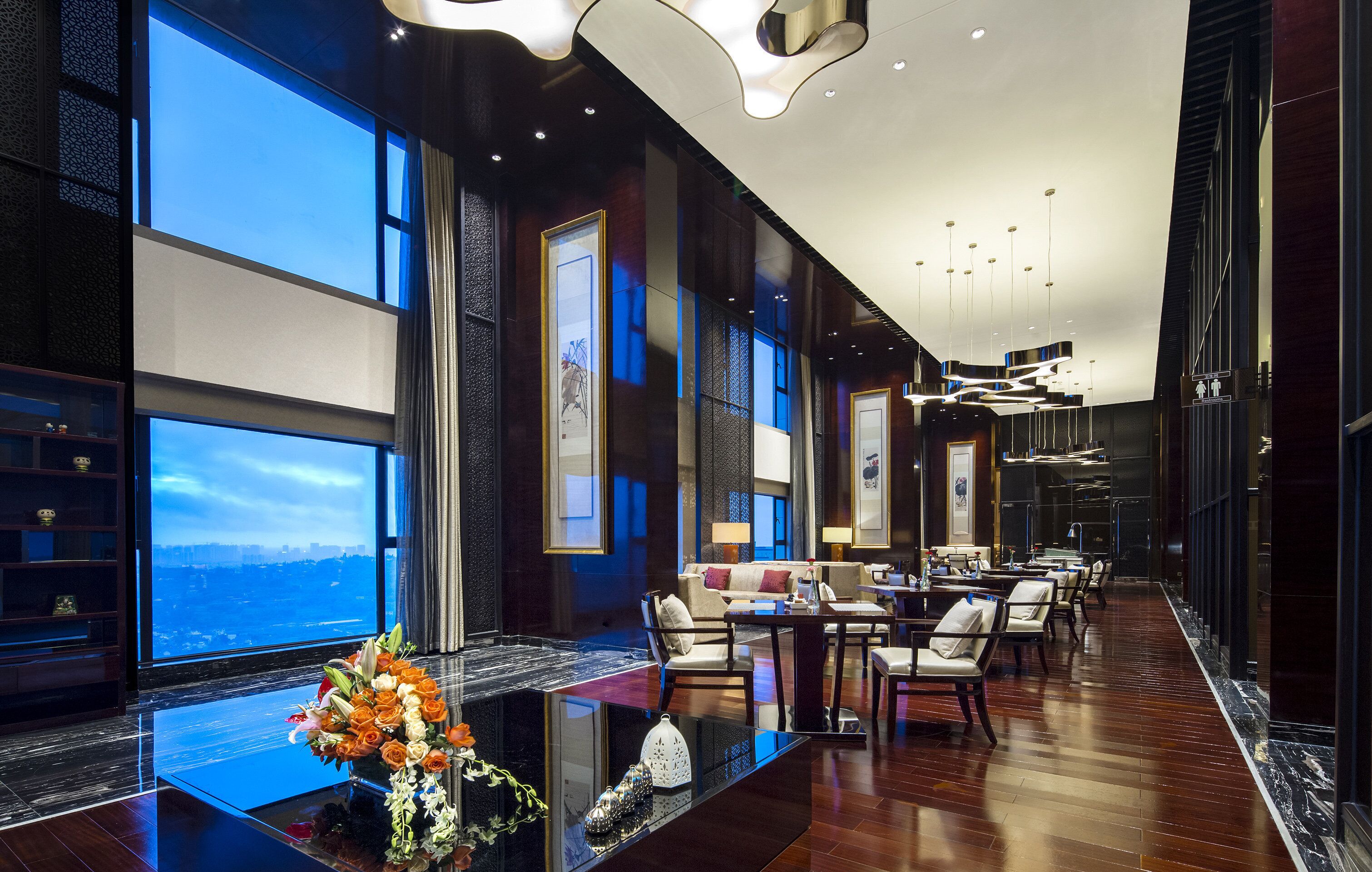 A modern hotel lobby with a long reception desk, seating area, and large windows offering a city view.