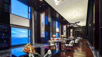 A modern hotel lobby with a long reception desk, seating area, and large windows offering a city view.