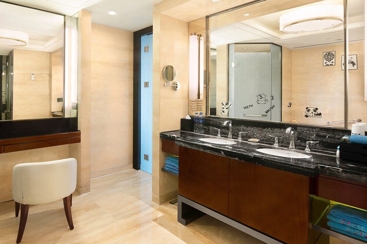 A modern bathroom with a vanity, two sinks, a mirror, and a toilet.