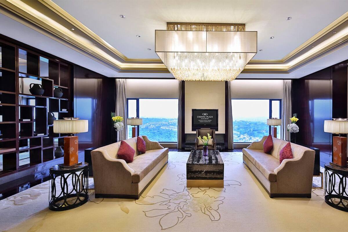 A spacious living room with two sofas, a large chandelier, and a view of the city.