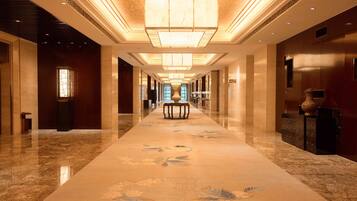 A long, well-lit hallway with a marble floor and floral patterns, leading to a large window at the end.