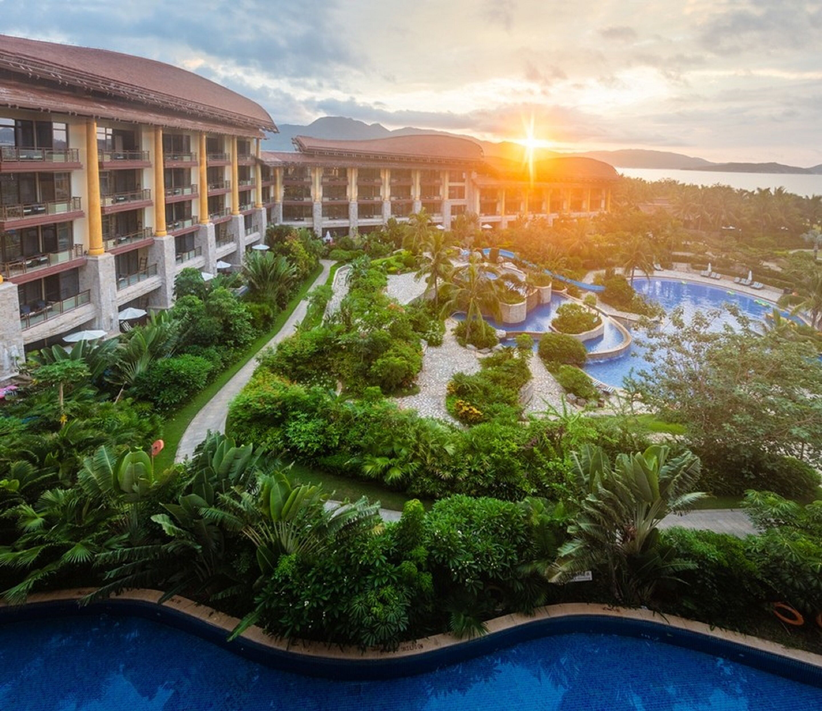A resort with a swimming pool, lush greenery, and a building with multiple balconies.