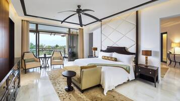 A modern hotel room with a large bed, a sitting area with a sofa and armchairs, a TV, and a balcony with a view.