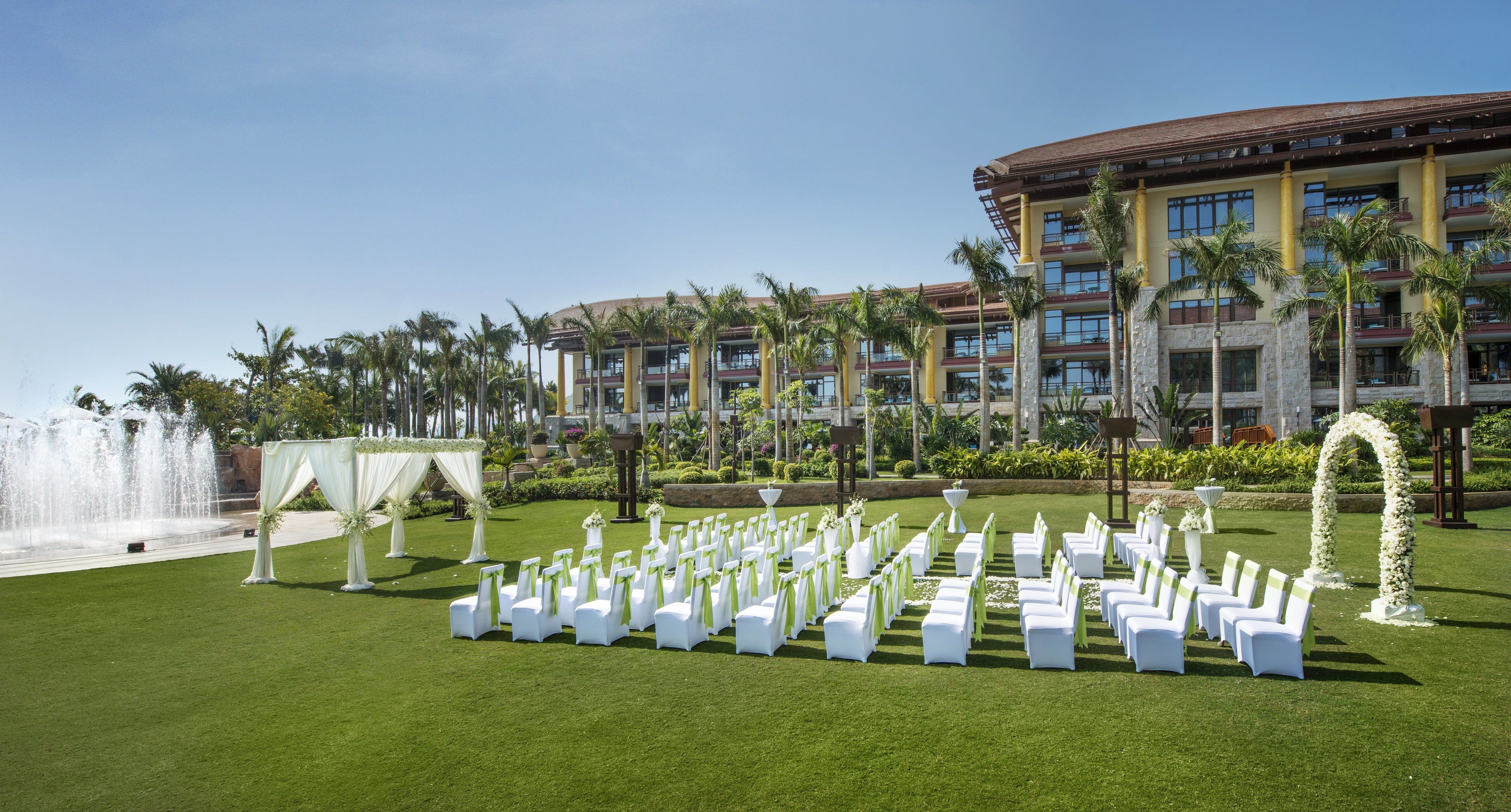 A hotel courtyard with rows of white chairs, a fountain, and a large building with multiple balconies and palm trees.