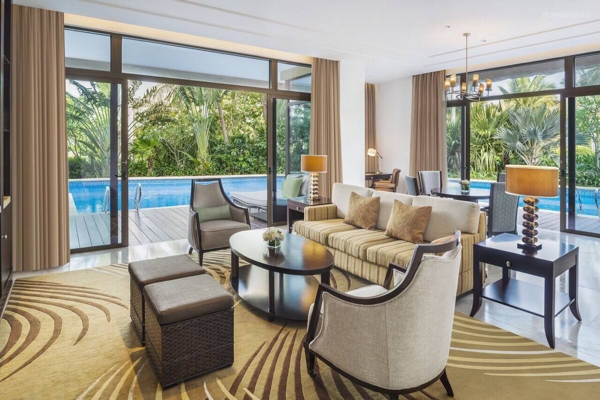 Un salon spacieux doté d’une grande fenêtre donnant sur une piscine, et aménagé avec un canapé, des fauteuils et une table basse.