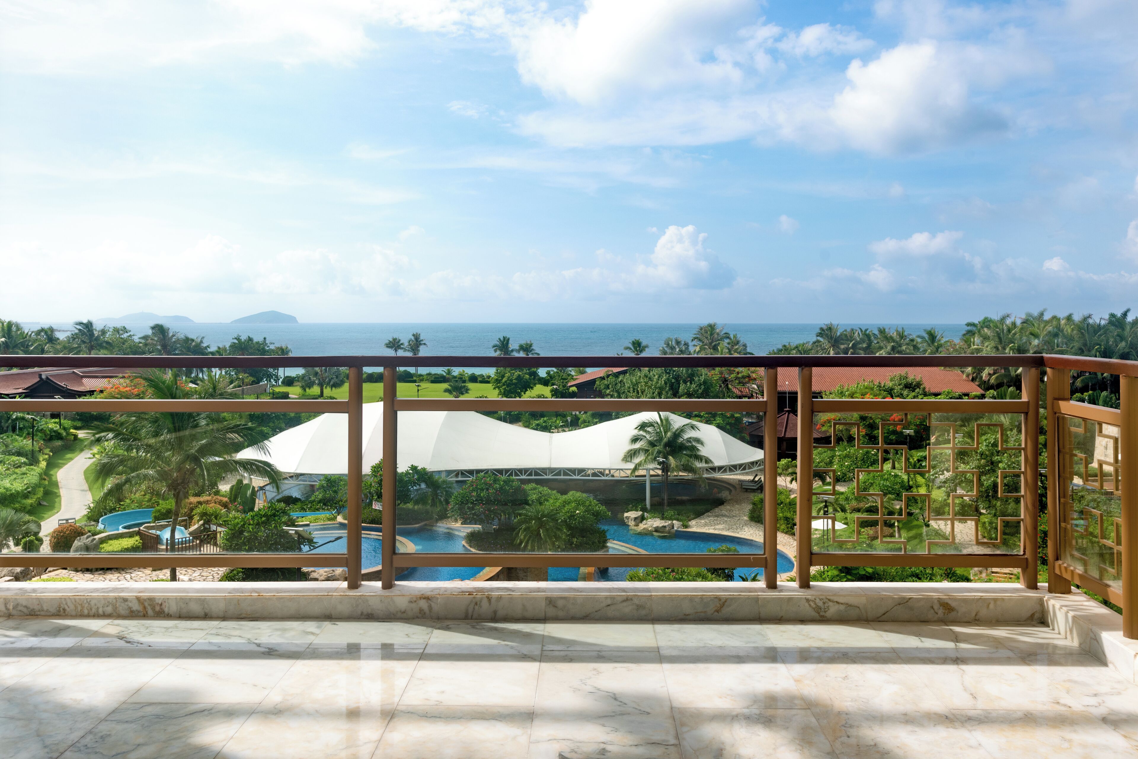 A balcony with a view of a pool, palm trees, and a distant island.
