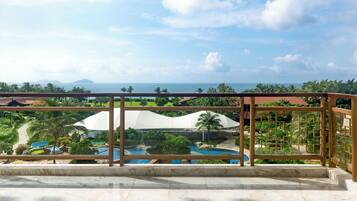 A balcony with a view of a pool, palm trees, and a distant island.