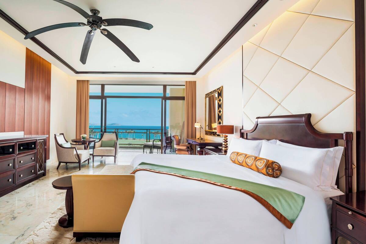 Une chambre d’hôtel avec un grand lit, un bureau, une chaise, un canapé et un balcon donnant sur la mer.